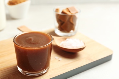 Glass with tasty caramel sauce and spoon on table. Space for text