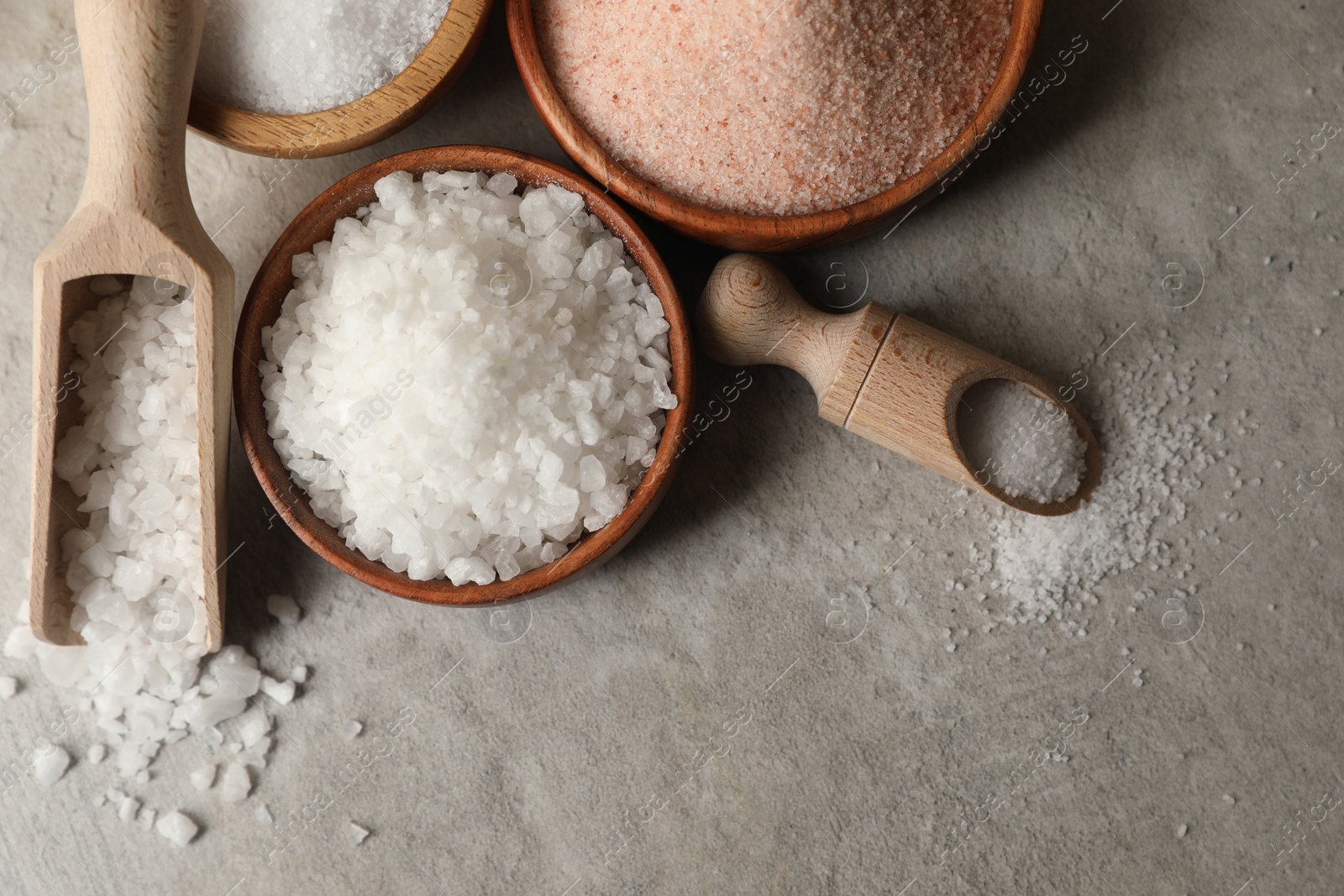 Photo of Different natural salt on grey textured table, flat lay. Space for text