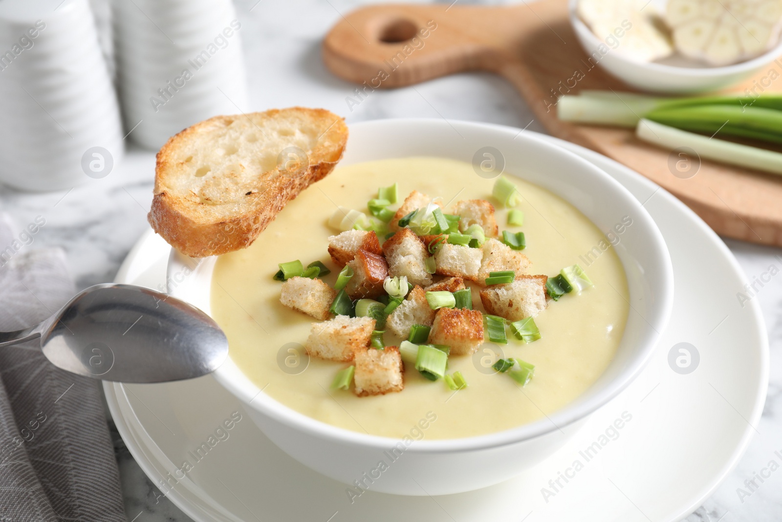 Photo of Tasty potato soup with croutons in bowl and spoon on white table