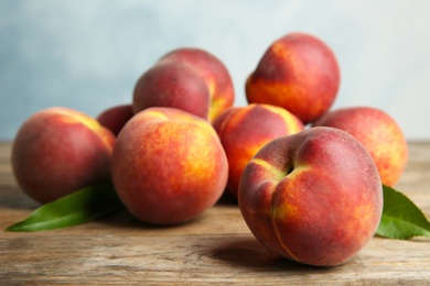 Photo of Fresh juicy peaches and leaves on wooden table against blue background