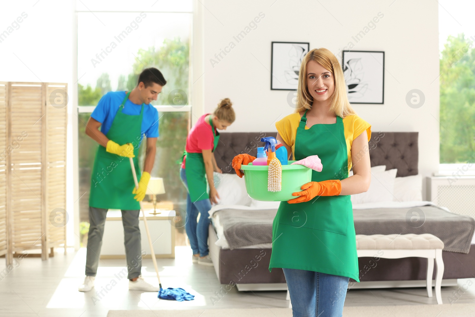 Photo of Team of professional janitors in uniform cleaning bedroom