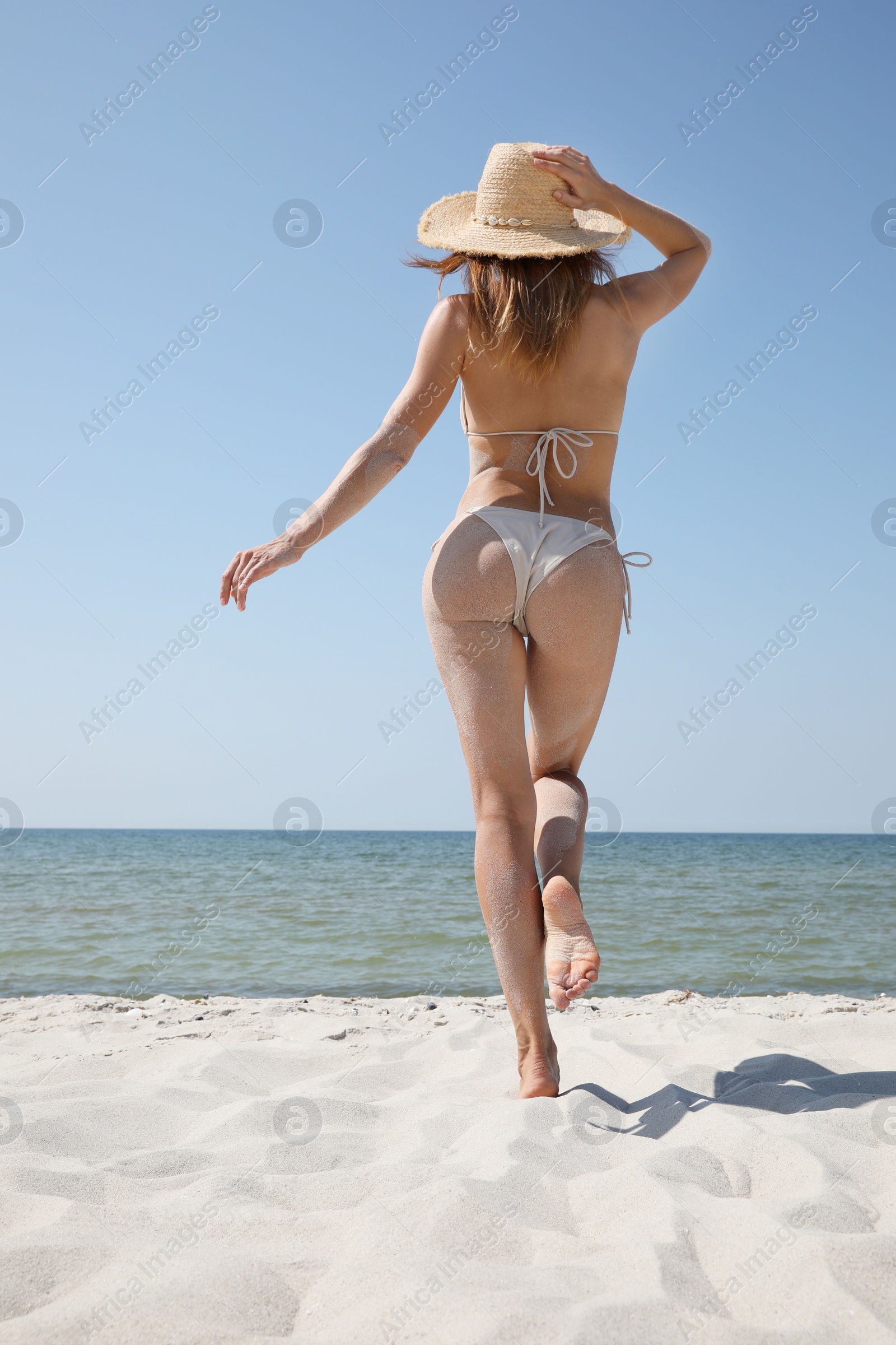 Photo of Woman with perfect body in bikini walking on sandy beach near sea, back view