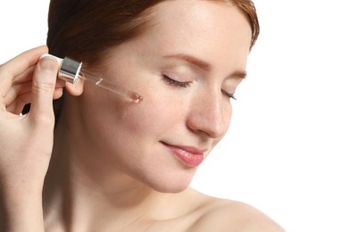Photo of Beautiful woman with freckles applying cosmetic serum onto her face on white background