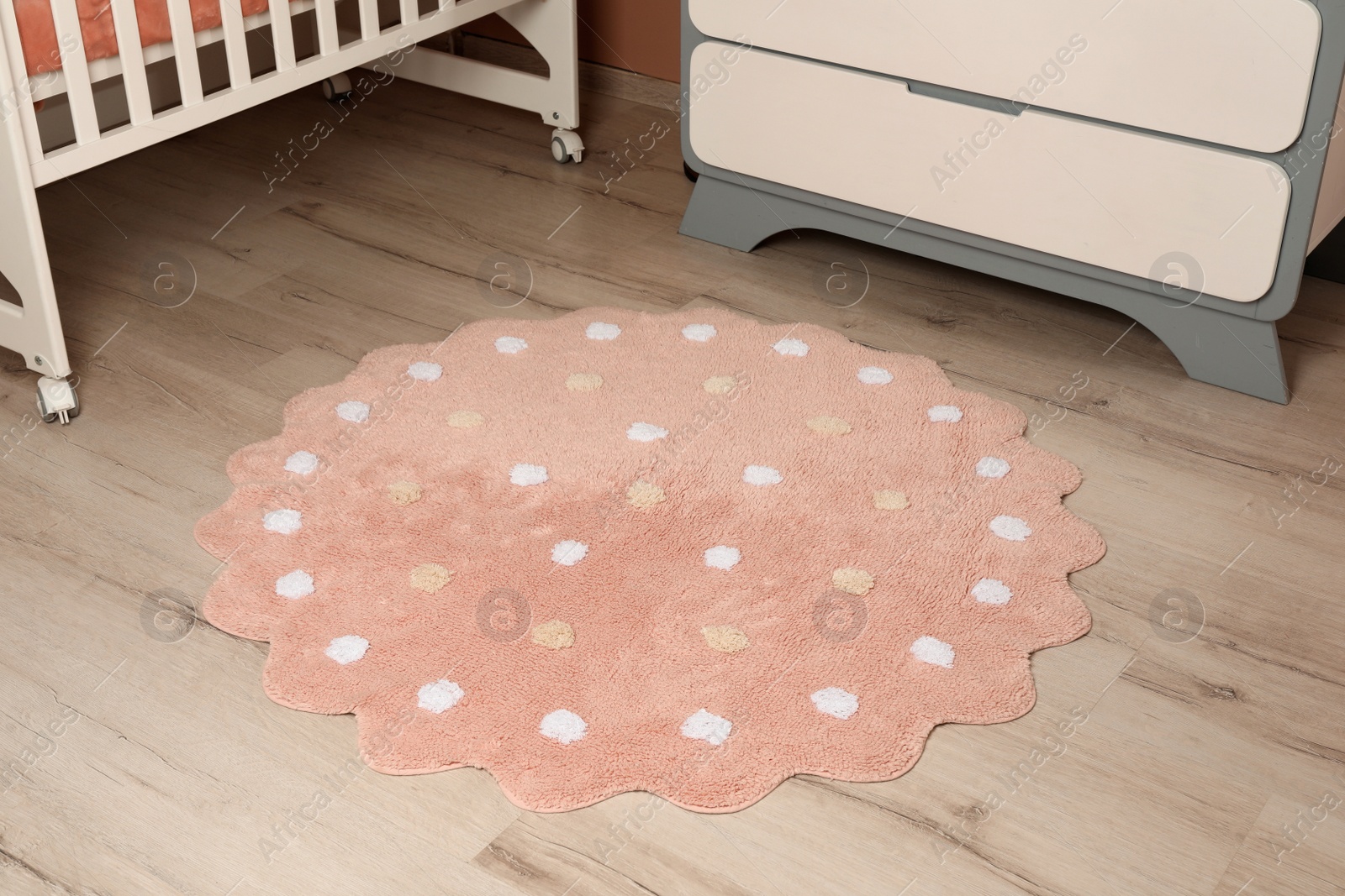 Photo of Round pink rug with polka dot pattern on wooden floor in baby's room