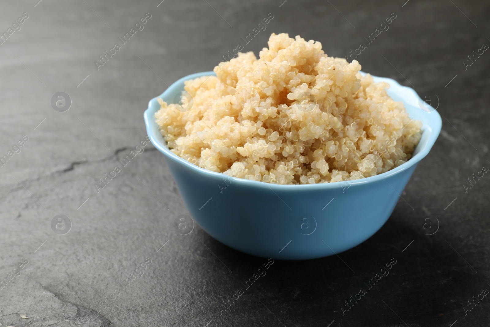 Photo of Tasty quinoa porridge in bowl on black textured table