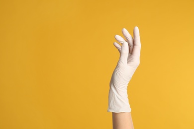 Doctor wearing medical gloves on yellow background, closeup. Space for text