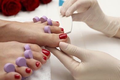 Photo of Pedicurist filing client`s toenails in beauty salon, closeup