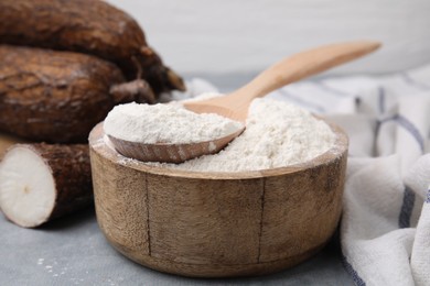 Photo of Wooden bowl and spoon with cassava flour on grey table, closeup