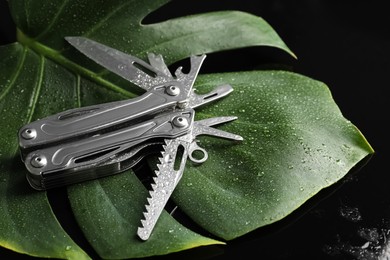 Photo of Compact portable metallic multitool with water drops on green leaf, closeup