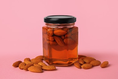 Photo of Jar with almonds and honey on pink background
