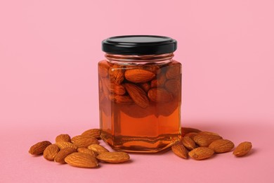 Jar with almonds and honey on pink background