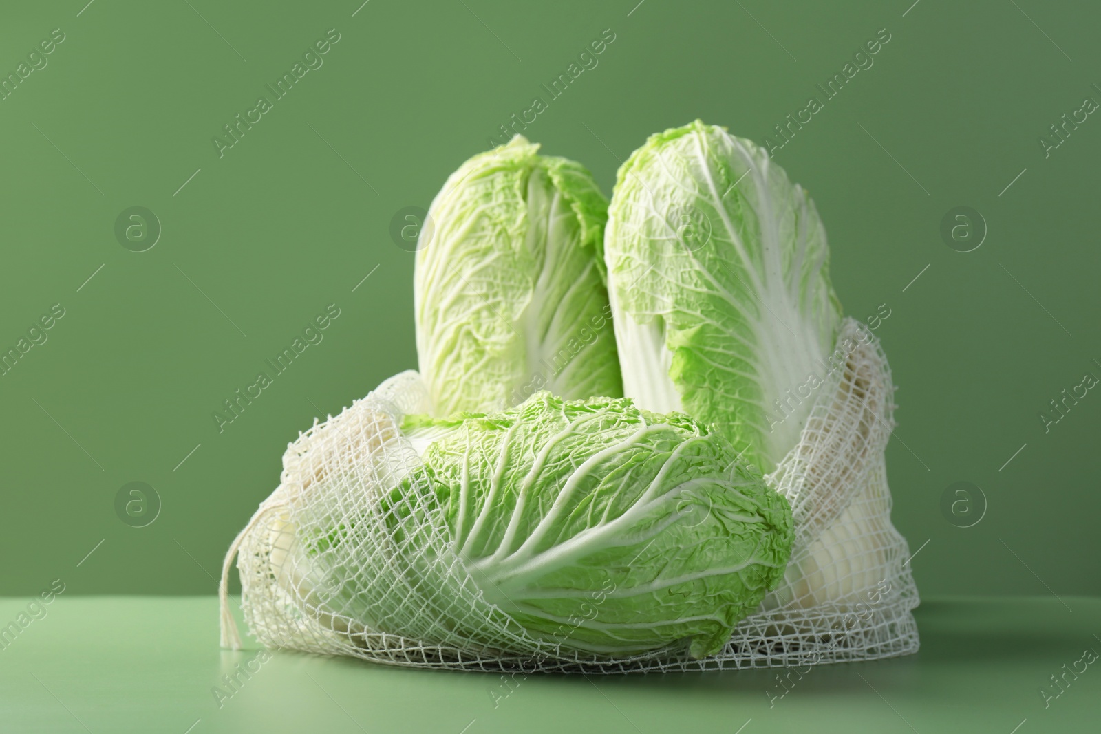 Photo of Fresh Chinese cabbages in string bag on green background