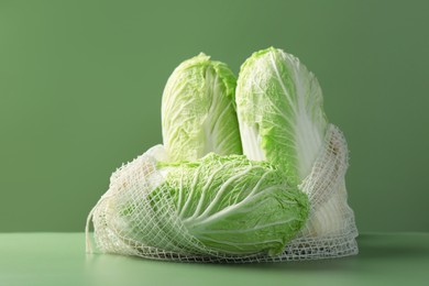 Photo of Fresh Chinese cabbages in string bag on green background