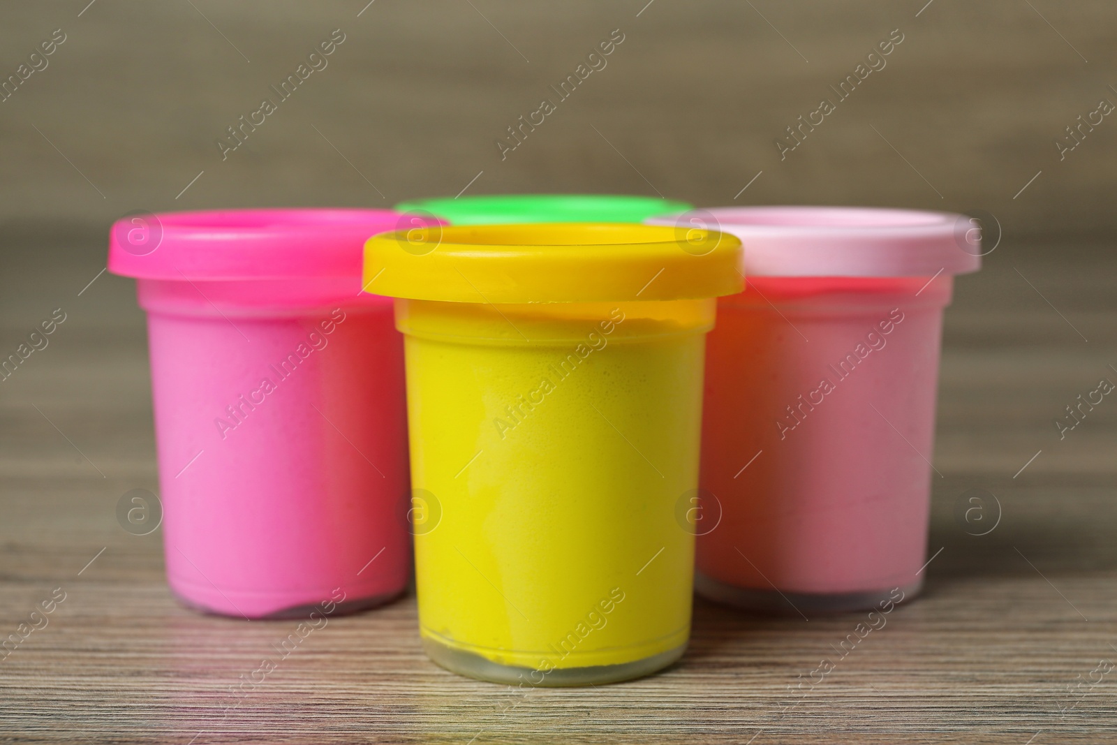 Photo of Plastic containers with colorful play dough on wooden table, closeup