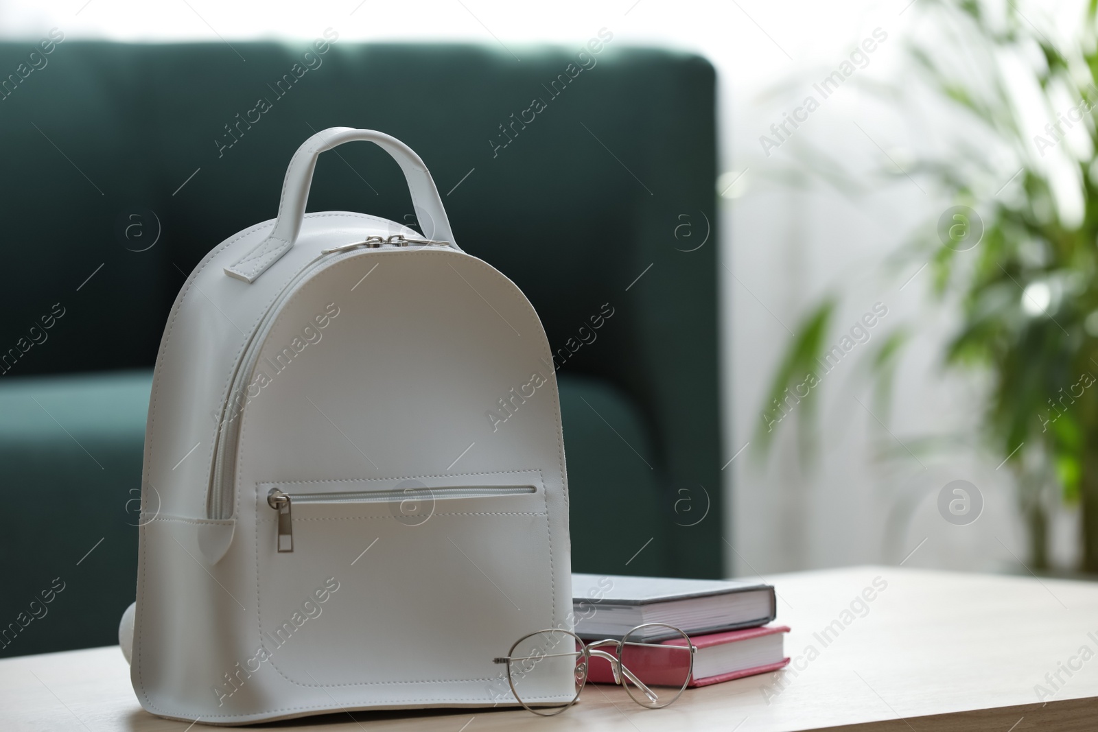 Photo of Stylish white backpack, notebooks and glasses on wooden table indoors, space for text