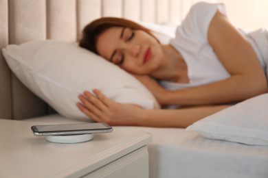 Smartphone charging on wireless pad and woman sleeping in bed