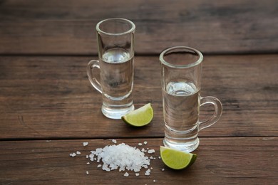 Mexican tequila shots with lime slices and salt on wooden table