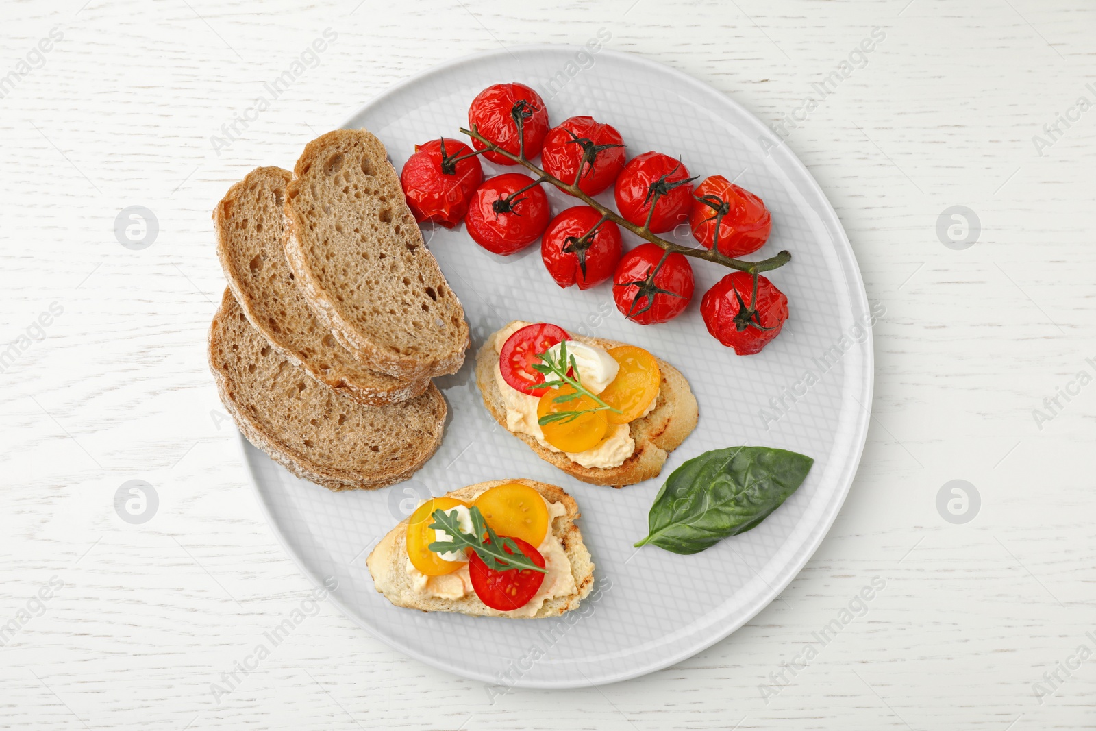 Photo of Plate of delicious tomato bruschettas on white wooden background, top view