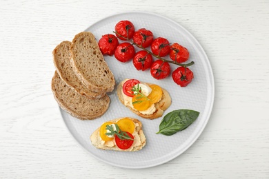 Photo of Plate of delicious tomato bruschettas on white wooden background, top view