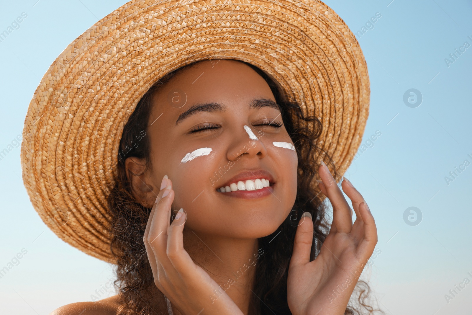 Photo of Beautiful African American woman with sun protection cream on face against blue sky