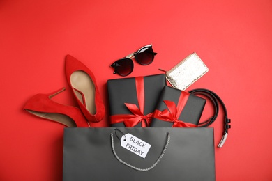 Shopping bag with gift boxes, shoes and women's accessories on red background, flat lay. Black Friday sale