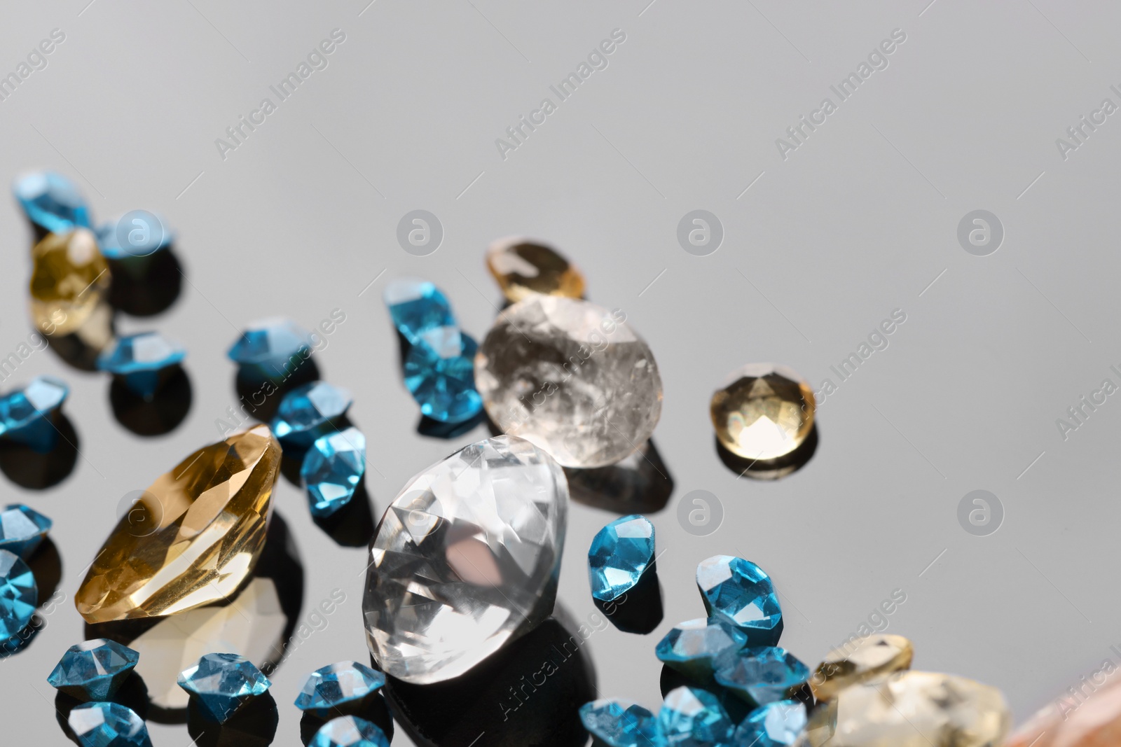 Photo of Different beautiful gemstones for jewelry on mirror surface, closeup. Space for text