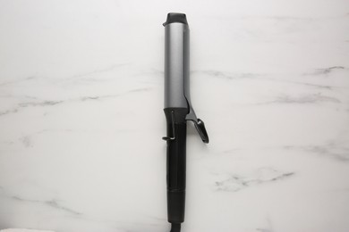 Photo of Hair curling iron on white marble background, top view