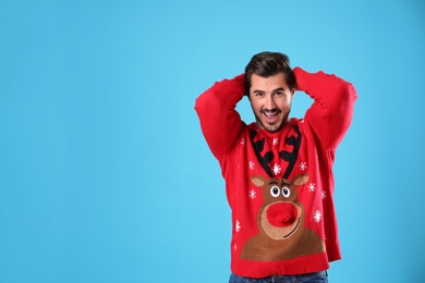 Portrait of happy young man in Christmas sweater on light blue background