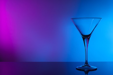 Photo of Empty clean martini glass on mirror table in neon lights, space for text