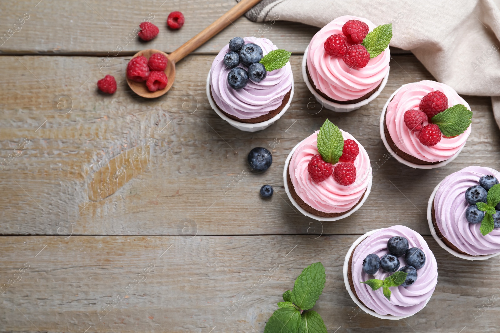 Photo of Sweet cupcakes with fresh berries on wooden table, flat lay. Space for text