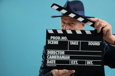 Photo of Senior actor holding clapperboard on light blue background, space for text. Film industry