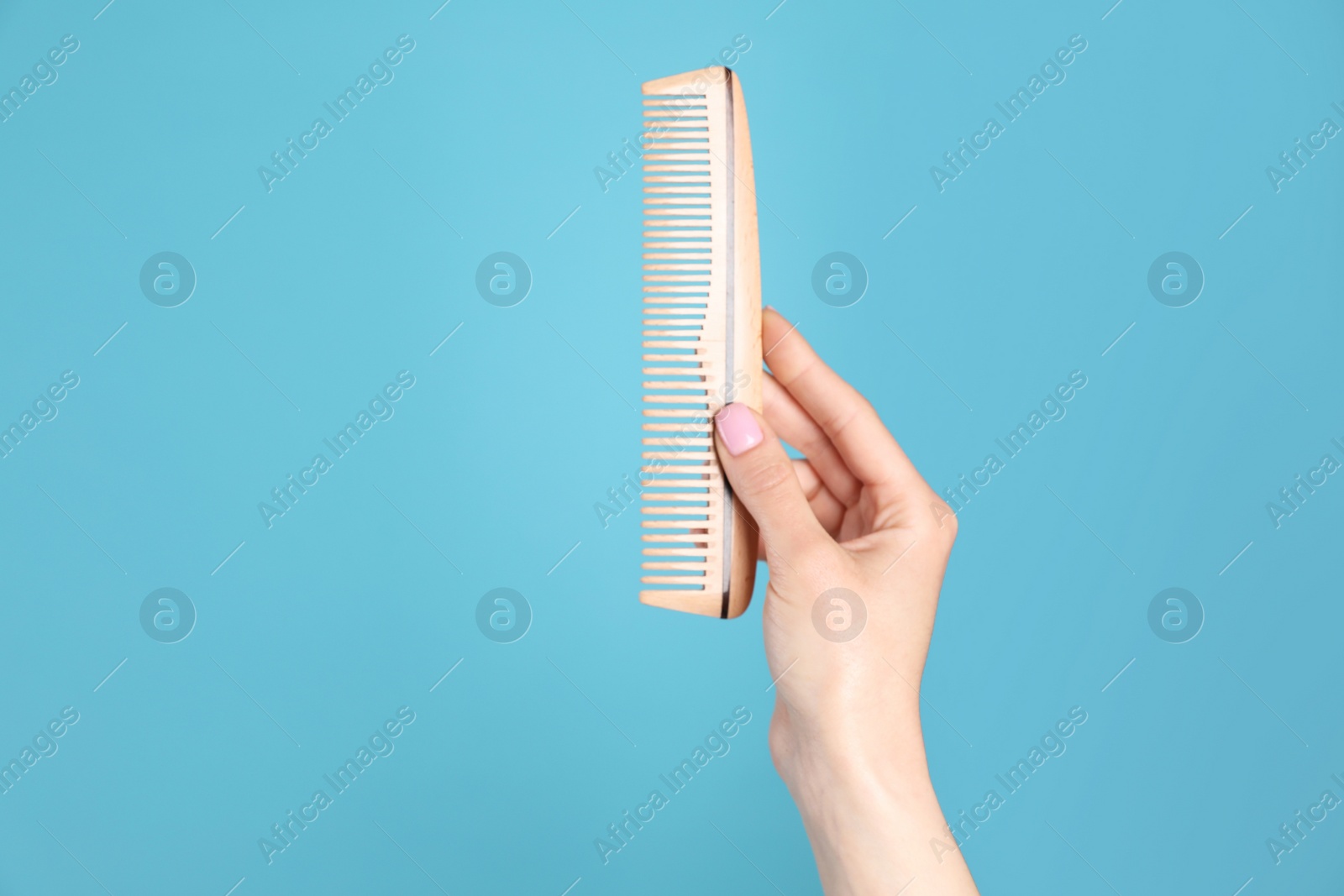 Photo of Woman holding wooden hair comb against blue background, closeup. Space for text