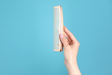 Photo of Woman holding wooden hair comb against blue background, closeup. Space for text