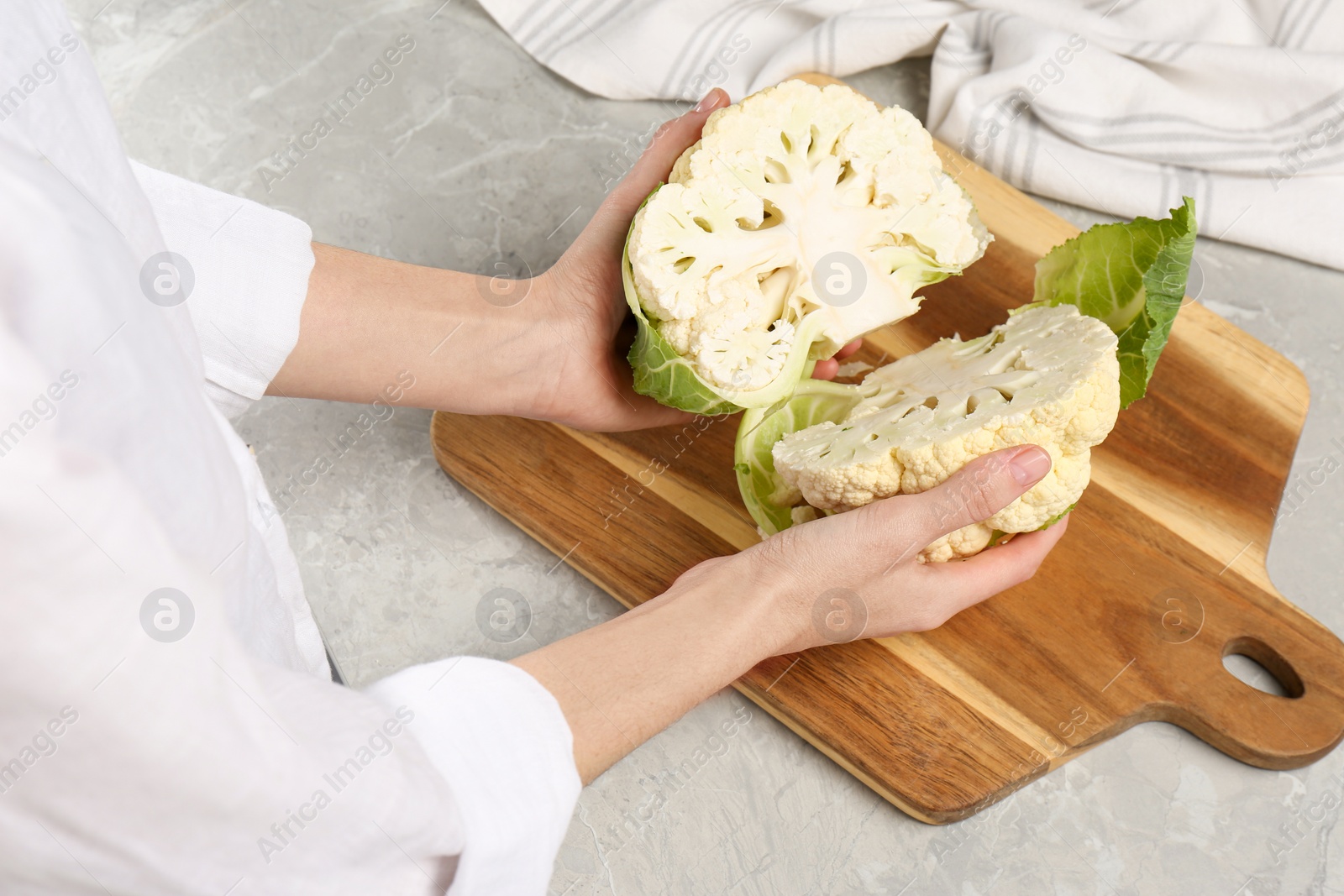 Photo of Woman with halves of fresh cauliflower at light grey table, closeup