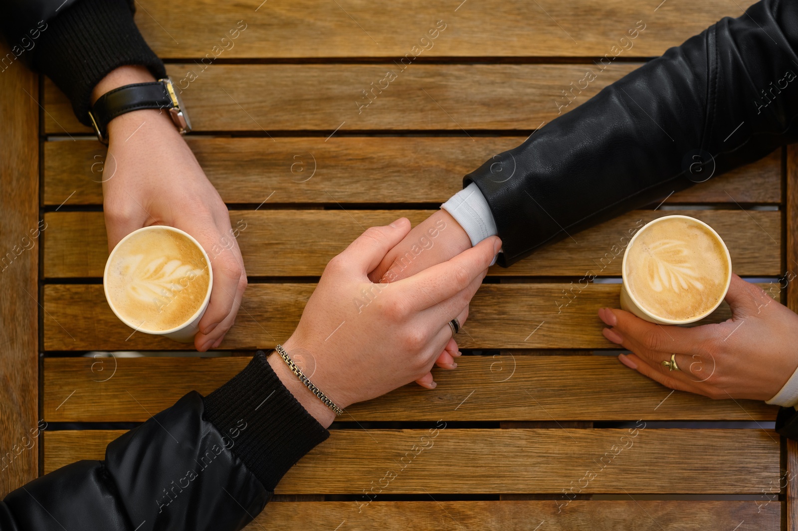 Photo of Lovely couple with coffee holding hands together at wooden table, top view. Romantic date