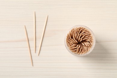 Disposable toothpicks and holder on white wooden background, flat lay