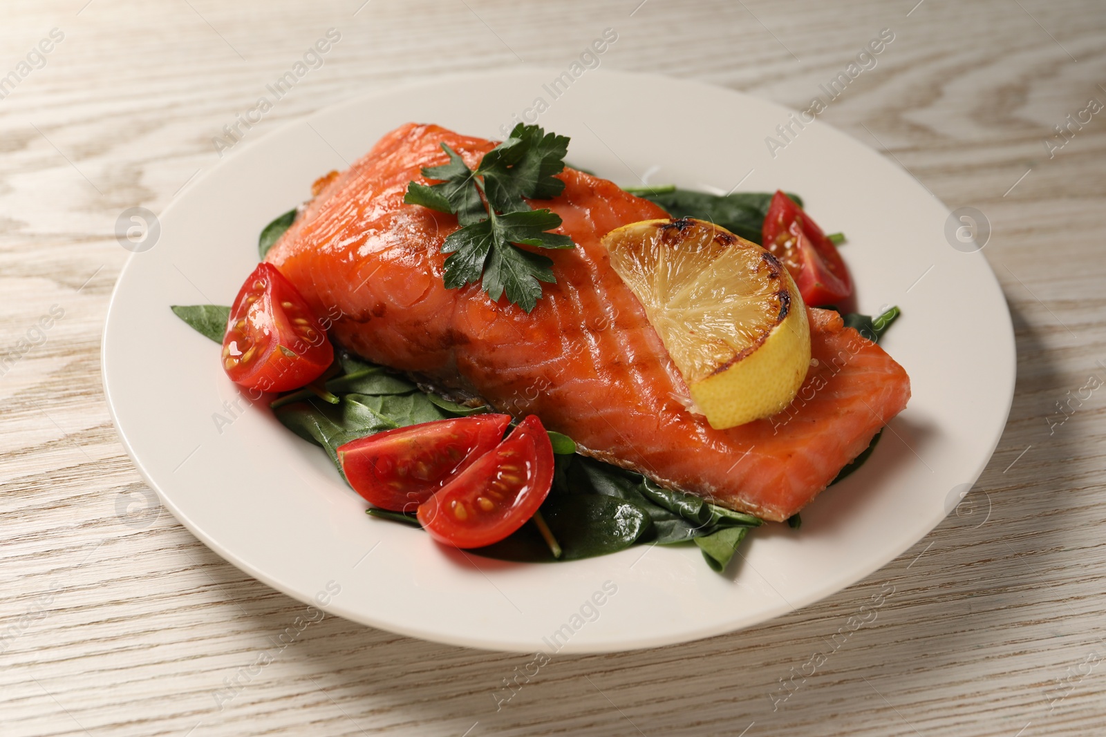 Photo of Tasty grilled salmon with tomatoes, lemon and basil on white wooden table, closeup