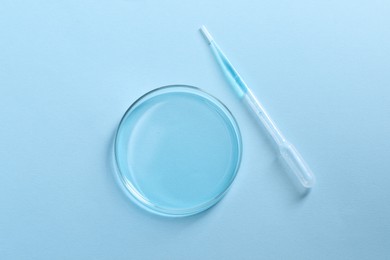 Photo of Transfer pipette and petri dish on light blue background, top view