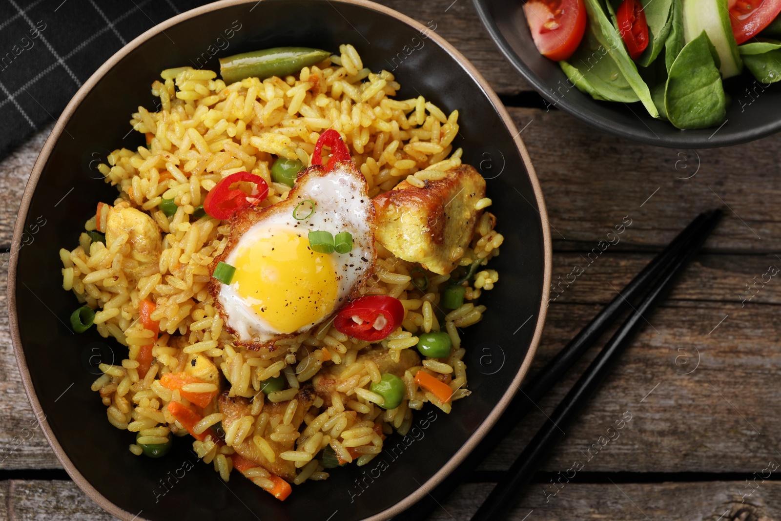 Photo of Tasty rice with meat, egg and vegetables in bowl served on wooden table, flat lay