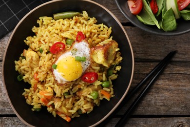 Tasty rice with meat, egg and vegetables in bowl served on wooden table, flat lay