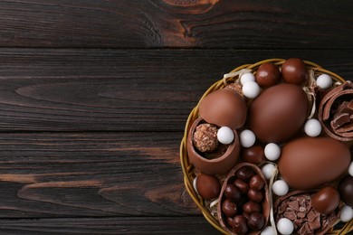 Photo of Tasty chocolate eggs and sweets in wicker basket on wooden table, top view. Space for text