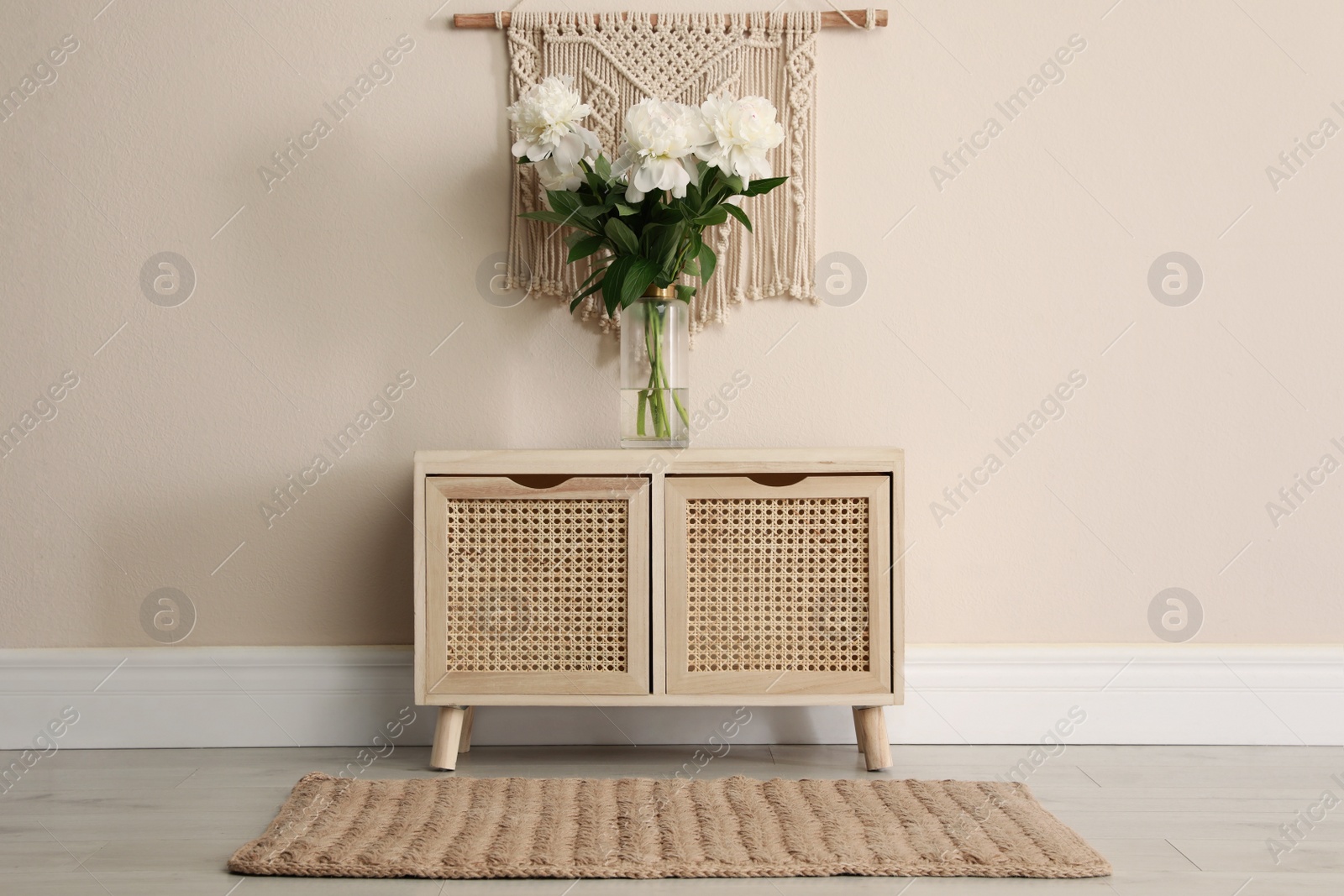 Photo of Wooden chest of drawers with bouquet near beige wall indoors
