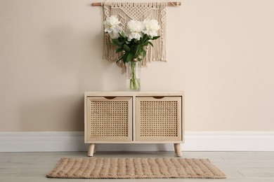 Wooden chest of drawers with bouquet near beige wall indoors