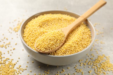 Photo of Millet groats in bowl and spoon on light grey table, closeup