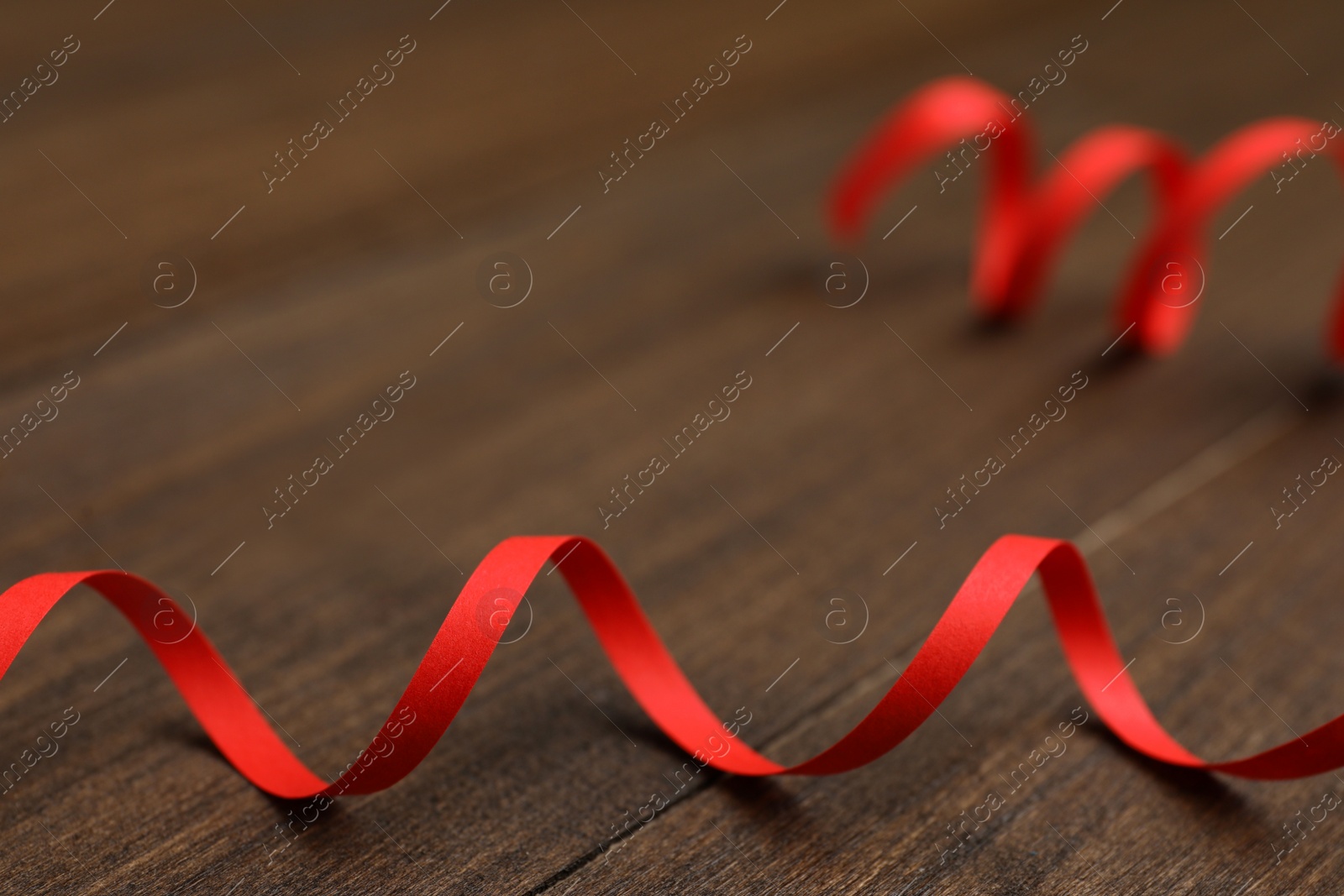 Photo of Red serpentine streamer on wooden table, closeup. Space for text