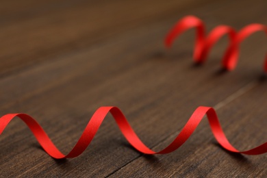 Photo of Red serpentine streamer on wooden table, closeup. Space for text