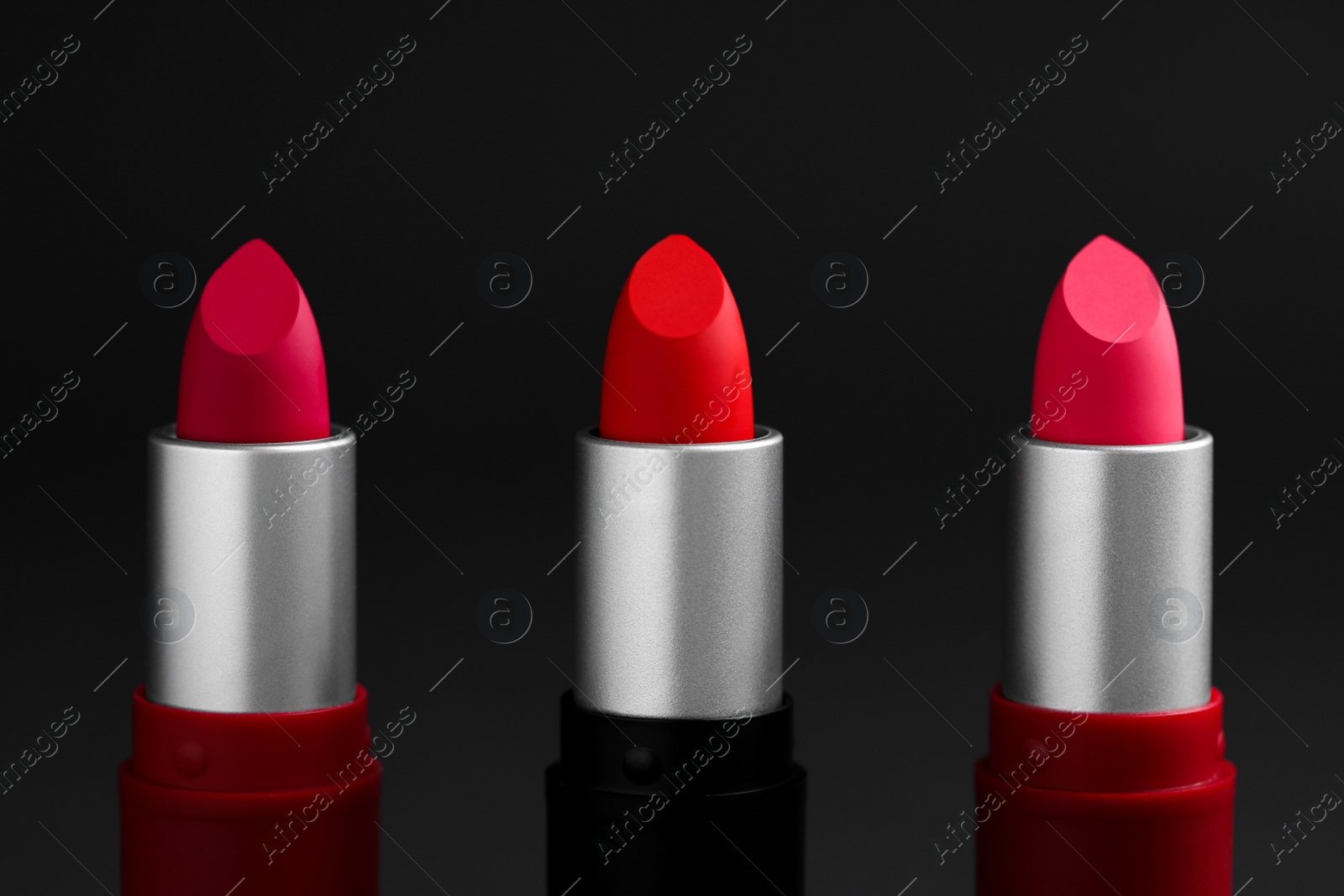 Photo of Different lipsticks on black background, closeup. Cosmetic product