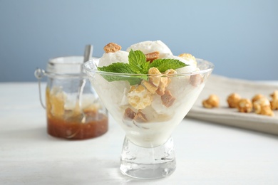 Delicious ice cream with caramel candies and popcorn in dessert bowl on white wooden table