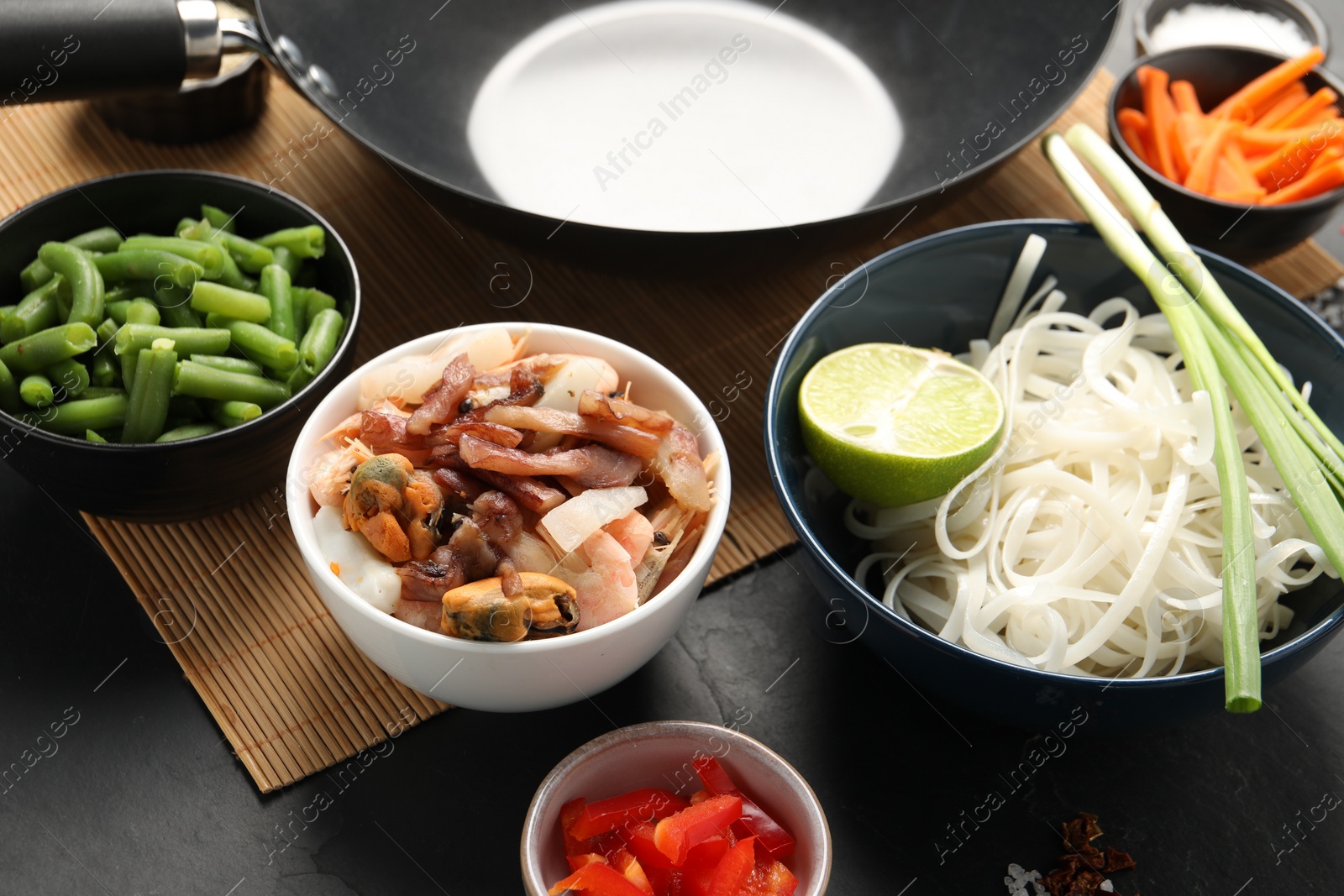 Photo of Black wok and products on dark table, closeup