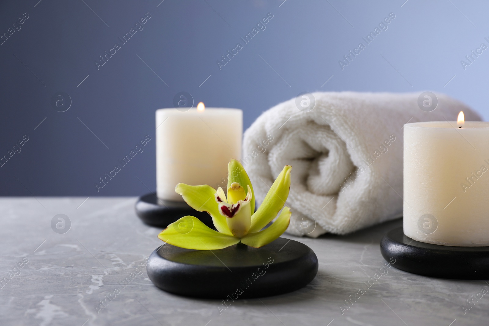 Photo of Spa stones with exotic flower and burning candles on grey table, space for text